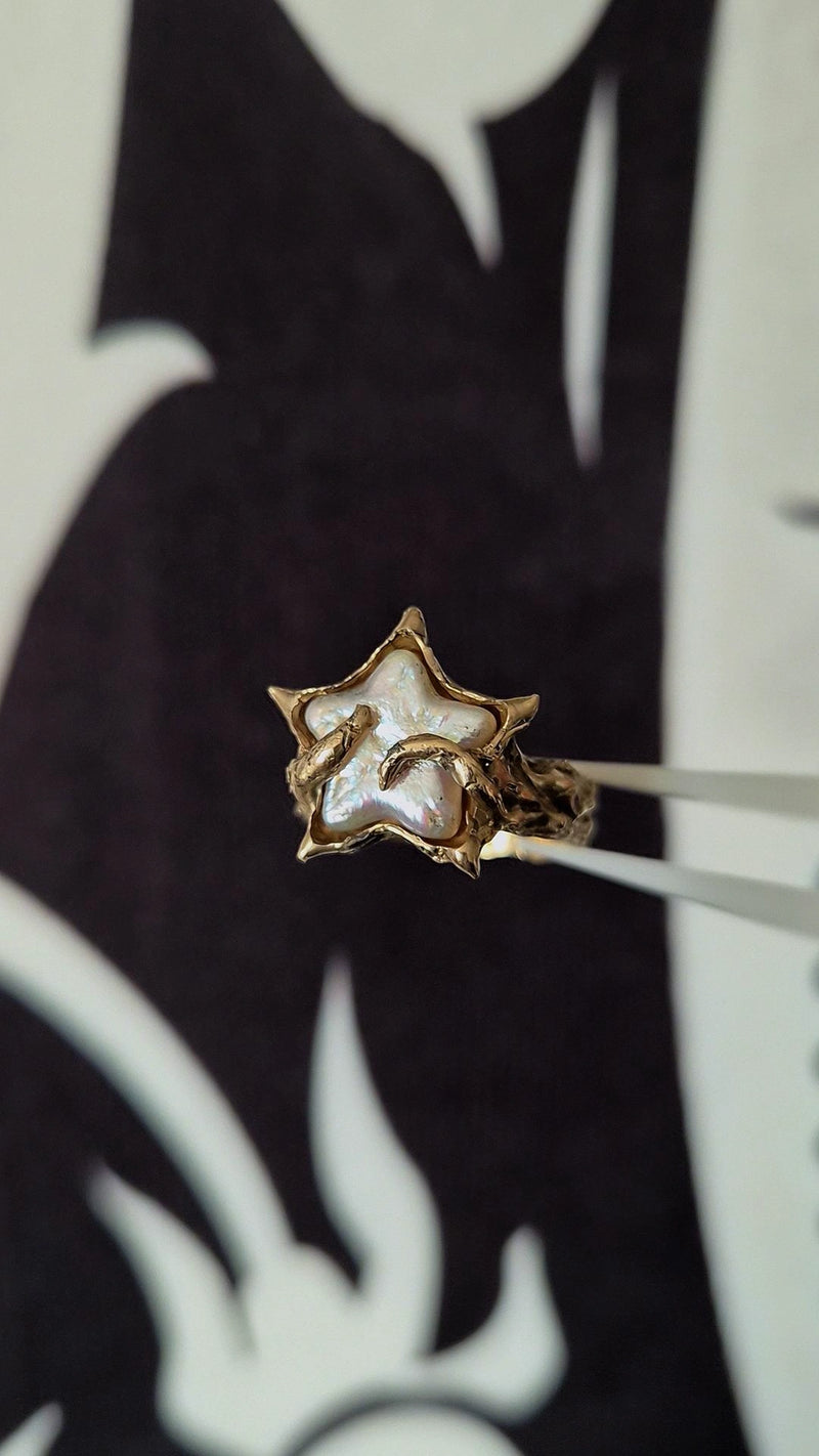 Gold ring with a star-shaped design held by tweezers against a black and white background