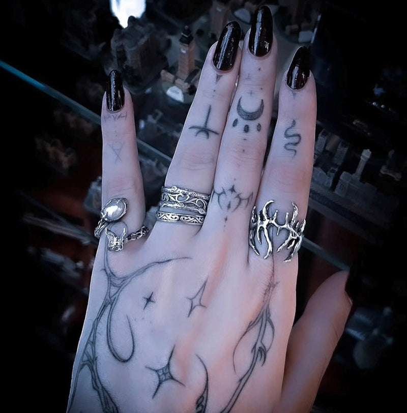 Hand with tattoos and multiple rings on a dark background, silver pearl ring