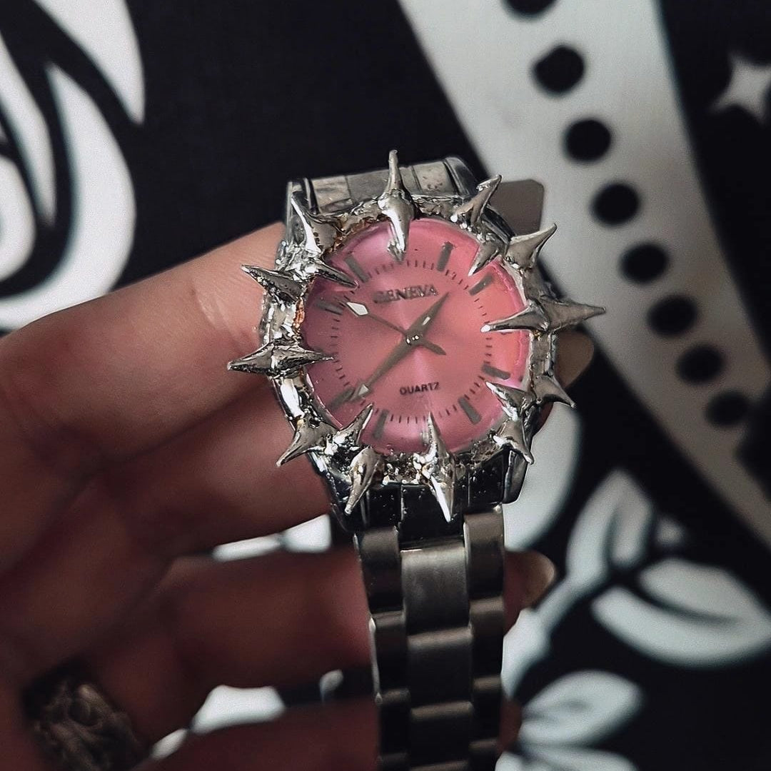 Pink and silver watch held by a hand against a black and white patterned background