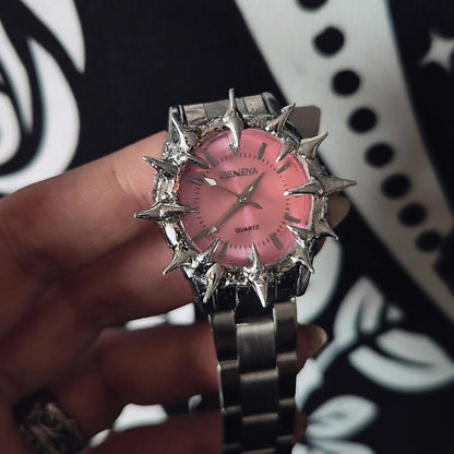 Pink and silver watch held by a hand against a black and white patterned background
