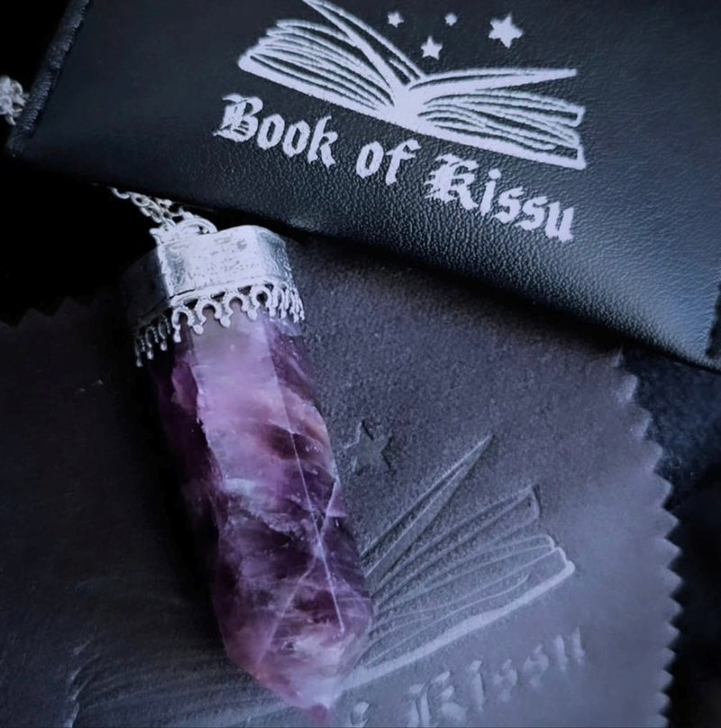 Purple crystal with decorative packaging labeled 'Book of Kitsu' on a dark background