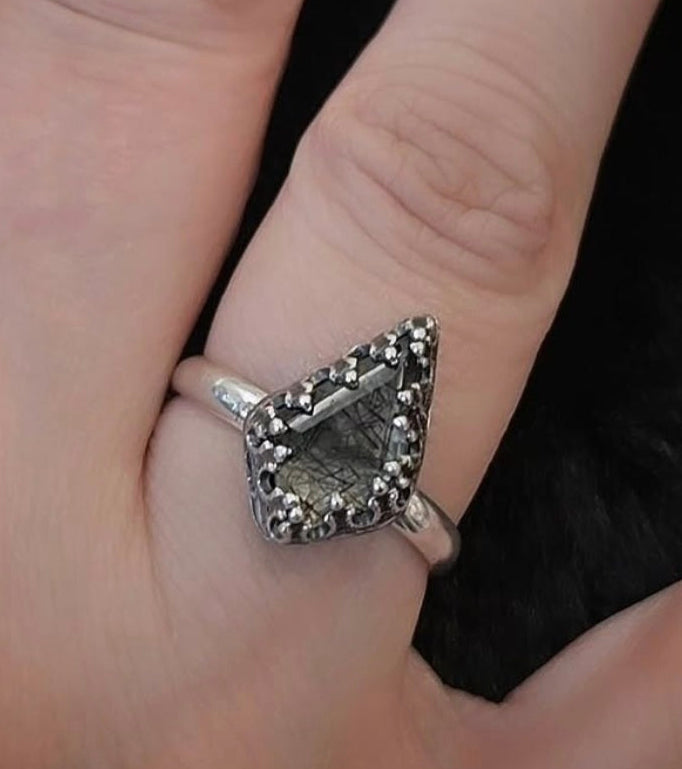 Silver ring with gemstone on a finger against a dark background