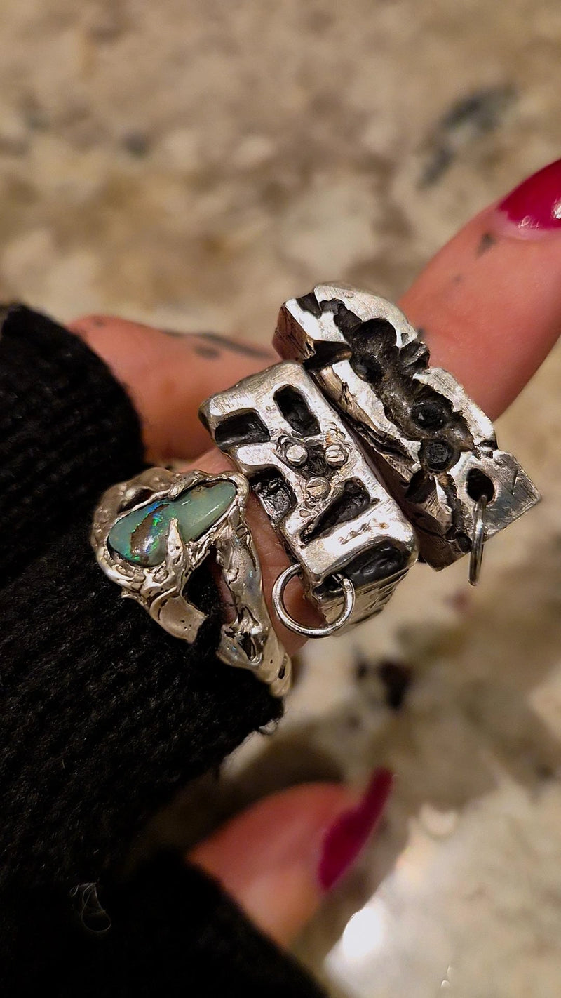 Close-up of a hand wearing multiple silver rings with intricate designs on a blurred background.