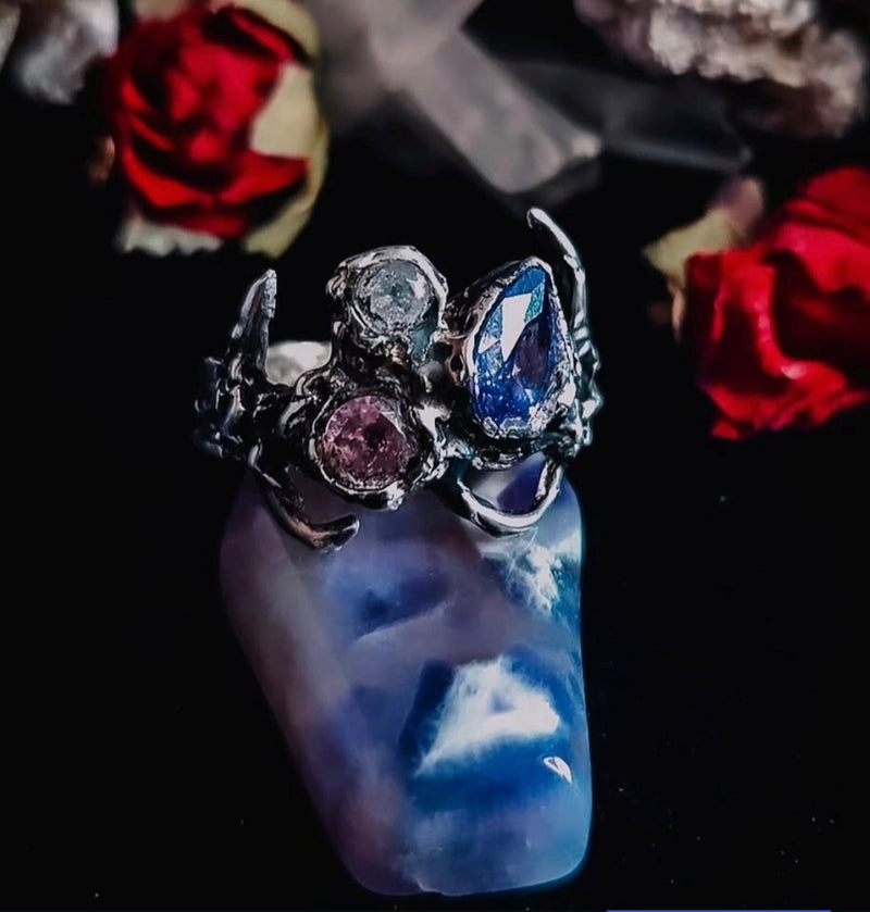 Silver ring with gemstones on a blue and white cloud-patterned object, surrounded by red roses.