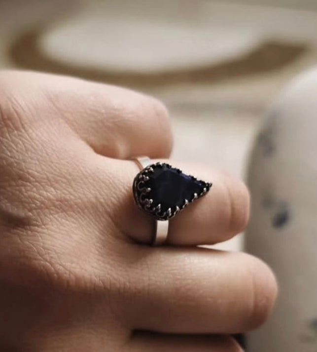 Hand wearing a ring with a lapis lazuli gemstone on a blurred background