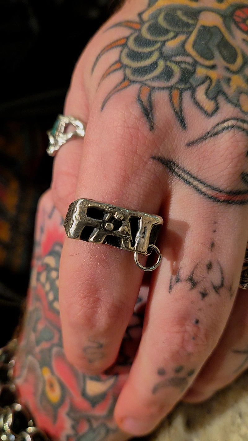 Hand with tattoos wearing a silver ring featuring a unique design.