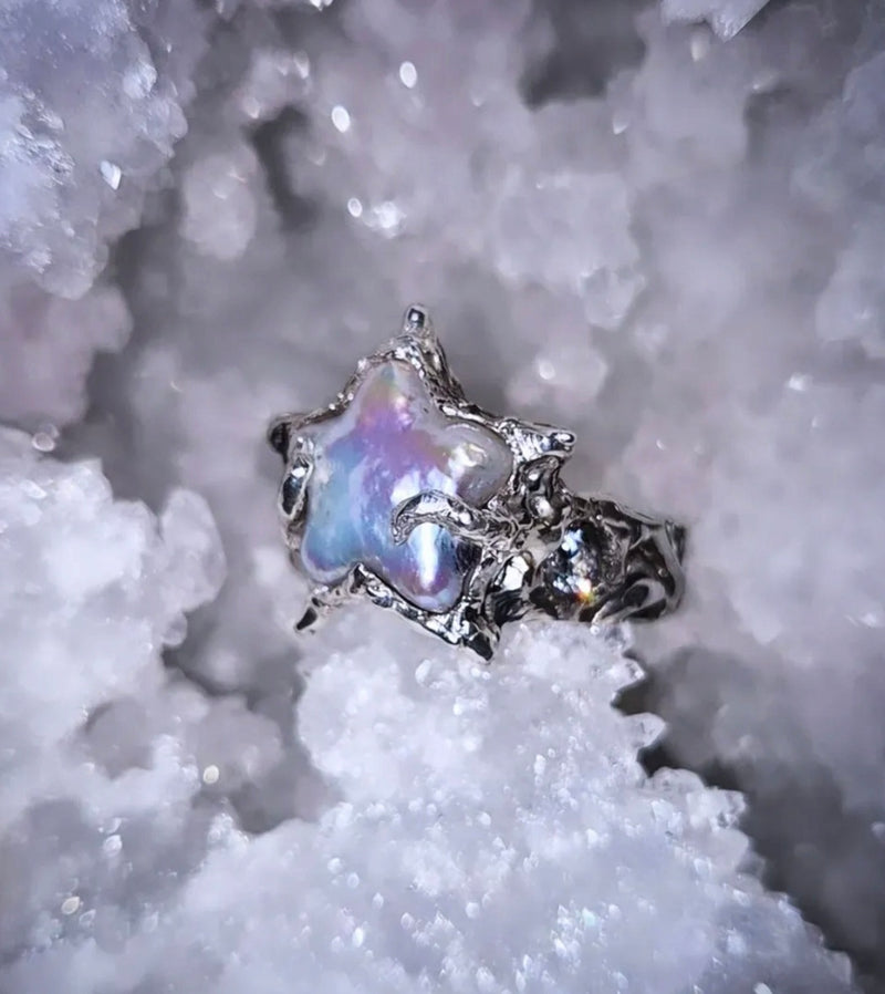 Star-shaped silver ring with iridescent center on a textured white background
