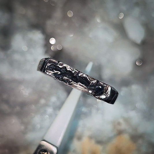 Silver ring with textured band on a blurred natural background