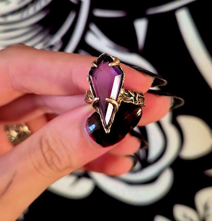 bronze ring with a purple gemstone held by a hand against a decorative background