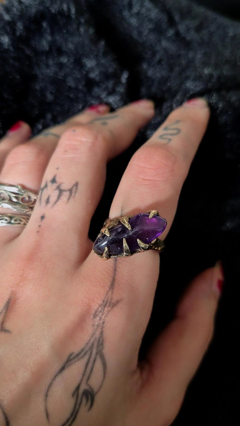Hand wearing an amethyst ring with tattoos on fingers against a dark background